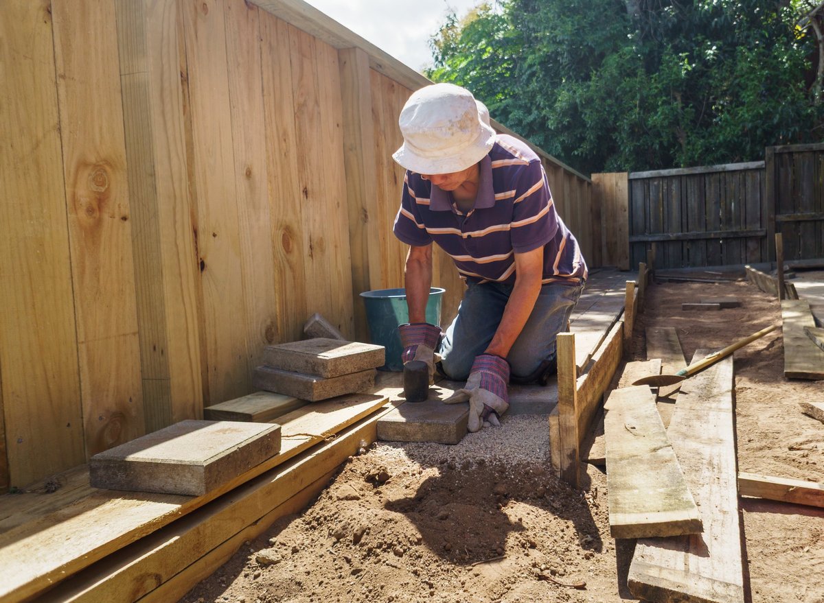Man laying brick pavers in the backyard garden